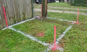 Boundary line survey showing property corners clearly marked with stakes and paint near a residential fence