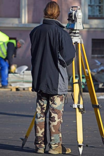 Land surveyor at road project - ALTA SURVEY Mississippi Land surveyor using a total station on a tripod to measure property boundaries near a street repair site