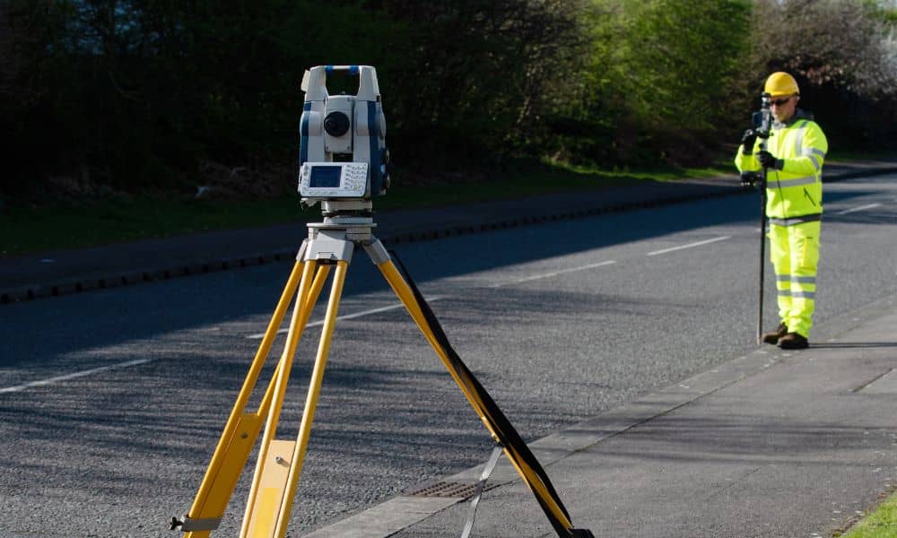 A land surveyor using a total station to collect data for topographic surveys during a road assessment