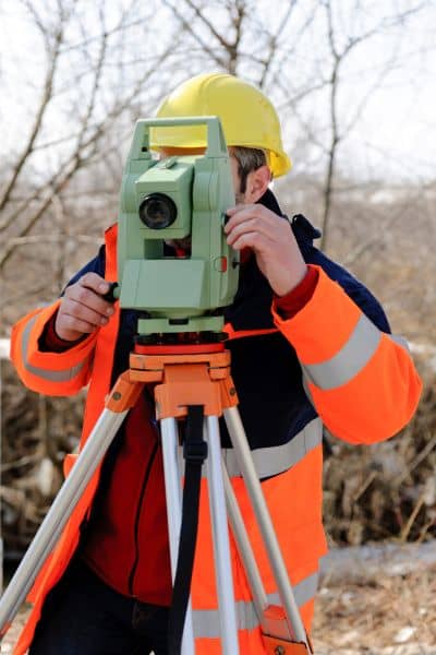 Land surveyor using a total station to measure accurate elevation data for flood map appeals