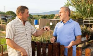 Two neighbors arguing over a fence line during a property boundary check by a licensed land surveyor