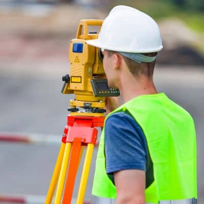 Licensed land surveyor measuring a property boundary using professional surveying equipment