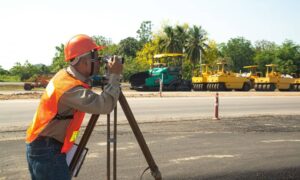 Land surveyor checking boundary near road project - ALTA SURVEY Mississippi Licensed land surveyor conducting an ALTA survey near a road construction site to verify property boundaries