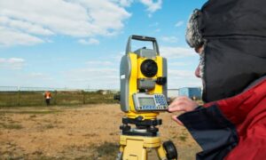 Surveyor using a total station to take measurements during a boundary survey on open land