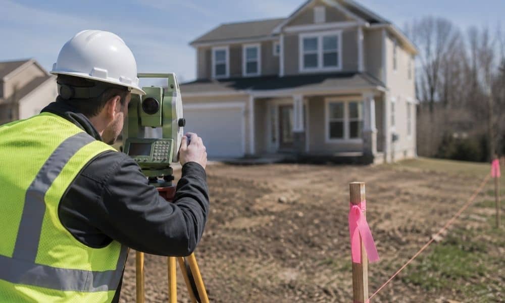 Licensed land surveyor using surveying equipment near a residential property to verify property lines and survey boundaries
