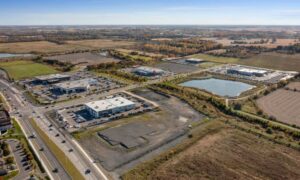 Aerial view of an industrial property with commercial buildings, parking areas, access roads, open land, and a stormwater pond