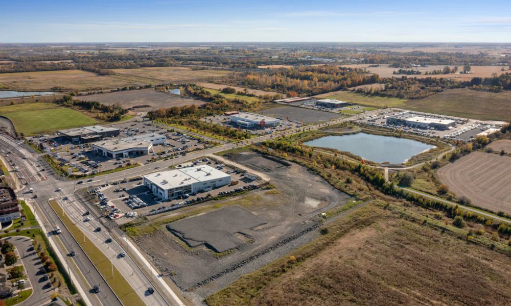 Aerial view of an industrial property with commercial buildings, parking areas, access roads, open land, and a stormwater pond